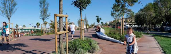 Bambina su monopattino in parco con passerella di legno.